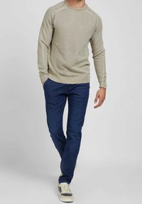 Pull tricoté vert clair avec encolure ronde, poignets et ourlet côtelés, associé à un jean bleu foncé et des baskets beiges.