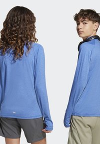 Modré tričká s dlhým rukávom, hladkou textúrou a raglánovými rukávmi, skombinované so sivými šortkami. Tričko má otvory pre palce na manžetách.