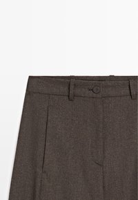 Pantalon en laine marron foncé avec passants de ceinture, fermeture par bouton caché et poches latérales sur fond blanc.