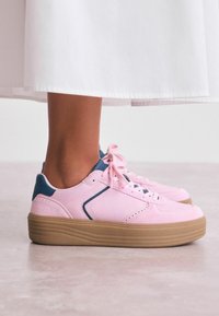 Sneaker rose avec une combinaison de daim et de cuir, dotée d'une semelle en caoutchouc gomme et d'accents bleu marine sur le talon et le côté.