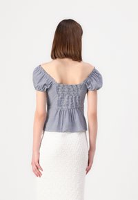 Top peplum a righe blu e bianche con maniche corte a palloncino e schiena smockata, abbinato a una gonna bianca texturizzata.