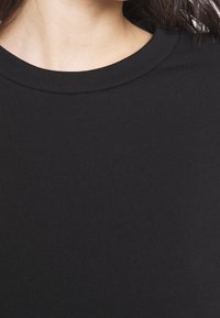 Černý bavlněný top s krátkými rukávy a kulatým výstřihem s hladkou texturou. Látka působí lehce a přiléhavě.