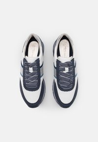 Bílé a námořnické tenisky s kulatou špičkou, texturovanými akcenty a vlnitým prostorem pro šněrování s více otvory na tkaničky.