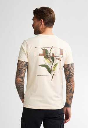 Camiseta de algodón color crema con un estampado botánico en la parte trasera, un logotipo rectangular y texto que dice "NORTHWOODS WISCONSIN U.S.A."
