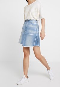 Jeanskjol i ljusblått med fransat fåll, sidoklyv och slitage. Kombinerad med en lös beige toppen och vita sneakers.