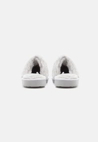 Witte, furry instap-slippers met een afgerond ontwerp, pluizige textuur en een zachte binnenvoering, met een platte grijze zool voor comfort.
