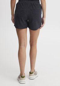 Svart terry-cloth shorts med elastisk midje, med en avslappet passform og buet kant, kombinert med lyse sneakers.