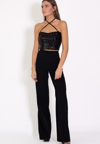 Top corto de lentejuelas negras con escote recto y tirantes cruzados, combinado con pantalones de campana negros de cintura alta. Textura brillante.