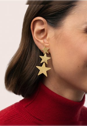 Pendientes de estrella con purpurina dorada, con tres formas de estrella descendentes, colgando de un pequeño pendiente de botón, usados sobre un fondo de suéter rojo.