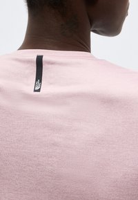 Κοντινό πλάνο ενός ατόμου που φοράει ανοιχτό ροζ πουκάμισο με κάθετη μαύρη λωρίδα με το λογότυπο "The North Face" κοντά στον αυχένα.