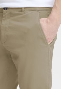 Light tan trousers made of smooth fabric, featuring side pockets and a button closure. The design is tailored with clean lines.