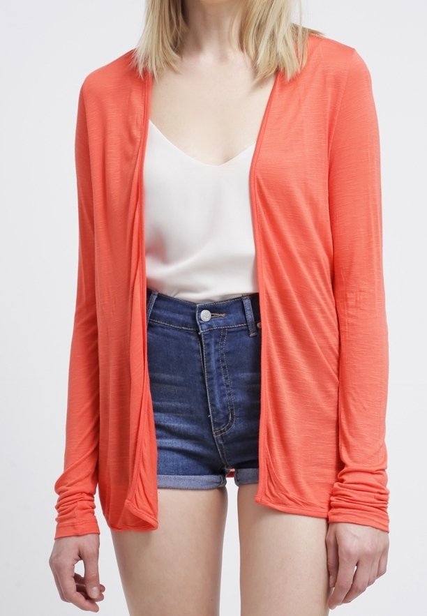 Coral lightweight cardigan with long sleeves, open front design, and soft texture, paired with a white top and denim shorts.