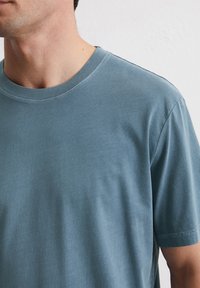 Kurzarm-T-Shirt aus gedämpften blauen Baumwolle. Klassisches Rundhals-Design mit weicher Textur und genähten Nähten, ohne Muster oder Grafiken.
