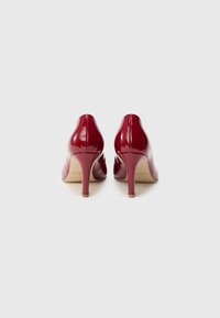 Chaussures à talons hauts en cuir verni rouge, avec un bout pointu et un talon fin et effilé, dotées d'une surface lisse et brillante et d'un design minimaliste.