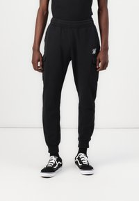 Black cargo sweatpants with an elastic waistband, side pockets, and cuffed ankles, paired with black and white sneakers.
