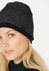 Sort strikket beanie med et struktureret mønster og ribkant. Har et lille sort logo-tag. Designet til varme og komfort.