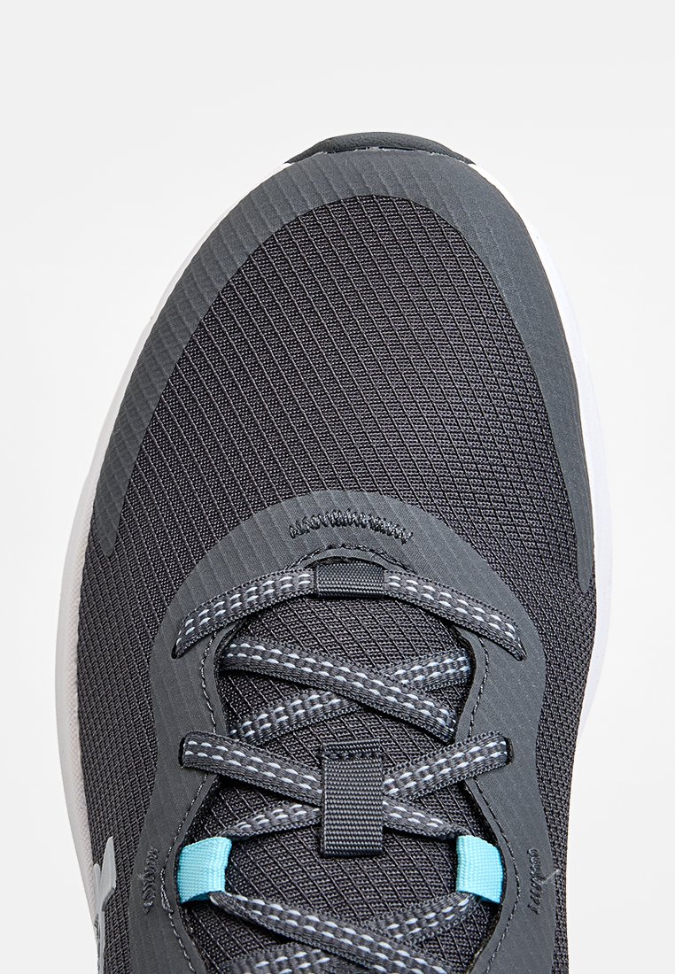 Zapatilla deportiva con parte superior de malla negra texturizada, acentos grises, cordones reflectantes y un ojal azul claro. Cuenta con una suela de goma blanca.