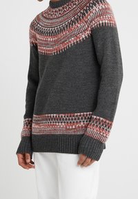 Pull en tricot gris avec un empiècement à motifs multicolores en rouge et blanc, avec des poignets et un ourlet côtelés.