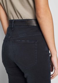 Mörka denimjeans med hög midja, subtila sömmar och en läderlapp med texten "DIESEL" bak. Fickor utformade i en klassisk form.