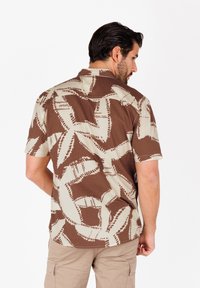 Camicia a maniche corte con un motivo astratto marrone e crema, tessuto a texture e colletto classico. La vista posteriore mostra la continuità del design.