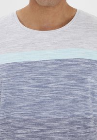 Grå og blå stribet T-shirt med rund halsudskæring; vandrette mønstre i lyseblå og mørkere blå; blødt, tekstureret stof.