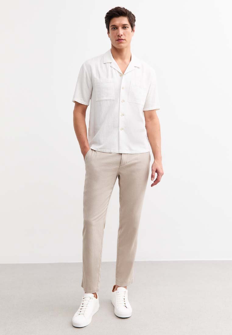 Kortärmad vit lin skjorta med två bröstfickor, parat med ljusbeige byxor och vita sneakers. Enkelt och avslappnat design.