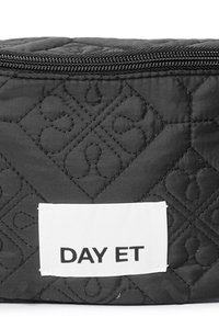 Mustikka musta kosmetiikkalaukku, jossa on kohokuvioitu kuvio. Valkoinen etiketti, jossa teksti "DAY ET." Vetoketjukiinnitys ylhäällä.