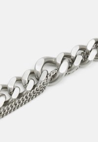 Cadena de metal plateado compuesta por grandes eslabones pulidos y una sección de eslabones más pequeños texturizados, que exhibe una mezcla de diseños lisos y retorcidos.