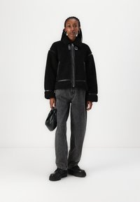 Zwarte fleecjas met een rits, hoge kraag en leren accenten. Gecombineerd met grijze wijde jeans en een zwarte handtas. Zwarte chunky schoenen.