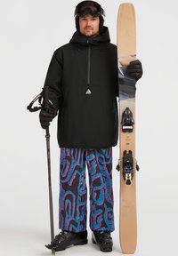 Zwarte waterdichte jas met een rits aan de voorkant, gestreepte paarse en blauwe sneeuwbroek, skischaatsen en ski's uitgerust met bindingen, vastgehouden naast een skistok.