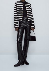 Veste tricotée rayée noir et blanc avec des boutons dorés, associée à un pantalon en cuir noir taille haute et des bottines ; petit sac à main noir.