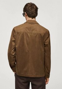 Veste en daim marron avec col, coupe droite et détails à boutons sur les manches. Texture lisse avec des coutures minimales.