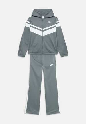 Grå Nike treningsdrakt med hvite chevron-striper på jakken og hvite sidepaneler på buksene, begge med Nike-logo.