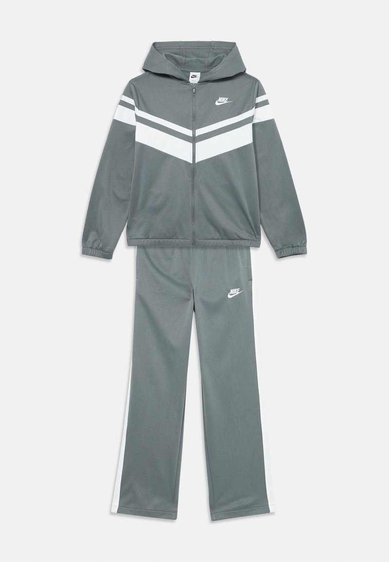 Sivi Nike trenirku s bijelim chevron prugama na jakni i bijelim bočnim panelima na hlačama, oboje s Nike logotipom.
