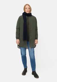 Groene gewatteerde parka met een rits, gecombineerd met een marineblauwe sjaal, blauwe jeans en zwarte enkellaarzen. Heeft een rechte snit en lange mouwen.