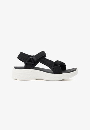 Sandalia negra de punta abierta con tiras ajustables y suela gruesa blanca acolchada diseñada para comodidad y uso casual.