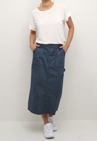 Falda midi de mezclilla con rayas verticales, dos bolsillos frontales y un bolsillo lateral. Combinada con una camiseta blanca de manga corta y zapatillas blancas.