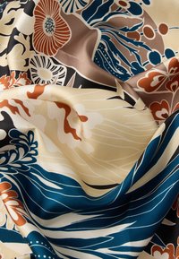 Floral fabric with a silky texture, featuring large blue, brown, and cream flowers on a beige background, with flowing leaf patterns.
