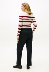 Maglione a righe con colori rosso e crema, abbinato a pantaloni blu navy. Scarpe nere. Vista da dietro che mostra la silhouette aderente e la trama a costine.
