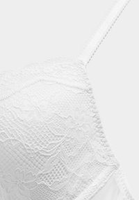 Witte kanten beha met bloemenpatronen, gestructureerde stof en verstelbare bandjes. Zachte, doorschijnende kant zorgt voor een delicate uitstraling.