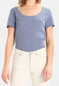 Short-sleeve, scoop-neck T-shirt in heathered blue cotton blend, paired with high-waisted off-white jeans, featuring a button closure and front pockets.