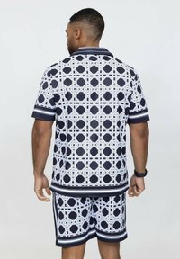 Ensemble de chemise à manches courtes et de shorts en bleu marine et blanc avec un motif géométrique, présentant une bordure rayée et une texture de tissu lisse.