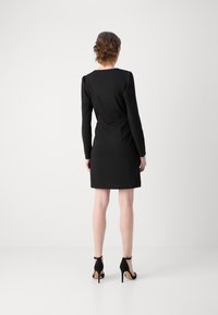 Robe noire ajustée à manches longues et col rond. Tissu lisse avec un design structuré, assortie de chaussures à talons hauts noires.