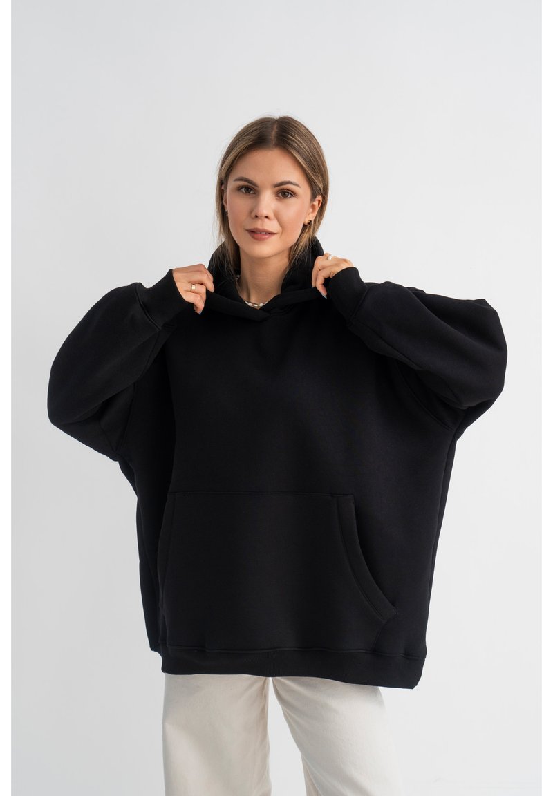 Felpa nera oversize realizzata in tessuto morbido, con cappuccio, tasca frontale e maniche lunghe. Design semplice senza fantasie o accenti.