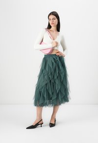Grønn tyllskjørt med volanger, paret med en hvit ribbet crop topp. Accessoriesert med en rosa skulderveske og svarte spisse sko.