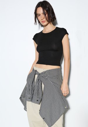 Haut court noir ajusté à manches courtes, associé à un foulard à carreaux avec des motifs en damier noir et blanc. Pantalon beige taille haute.