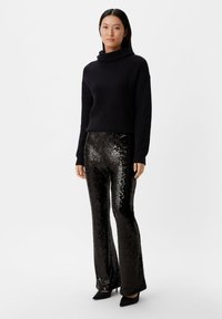 Zwarte gebreide coltrui met ribbeltextuur, gecombineerd met zwarte pailletten flared broek en zwarte puntige hakken.
