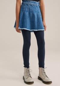 Denim krilo v stilu skater s razpokanimi robovi, v kombinaciji z mornarskimi legingami in bež vezalkami do gležnjev. Ima prilega pas in nabran dizajn.