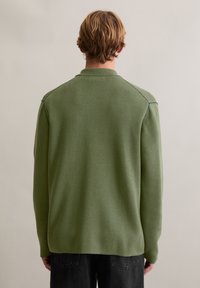 Zielony pulower z dzianiny z kołnierzem, długimi rękawami i prostym dołem. Charakteryzuje się fakturowanym wykończeniem oraz raglanowymi szwami na ramionach.