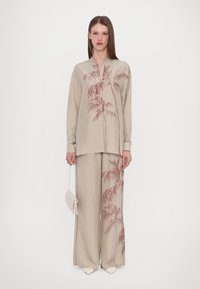 Světlobéžový outfit skládající se z dlouhého rukávu košile s růžovými botanickými vzory a širokými kalhotami; doplněno malou, světlou kabelkou.